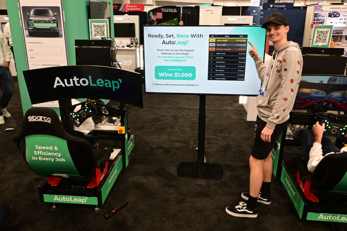 Attendee points to the F1 Simulator Challenge leaderboard at the AutoLeap booth, SEMA 2025