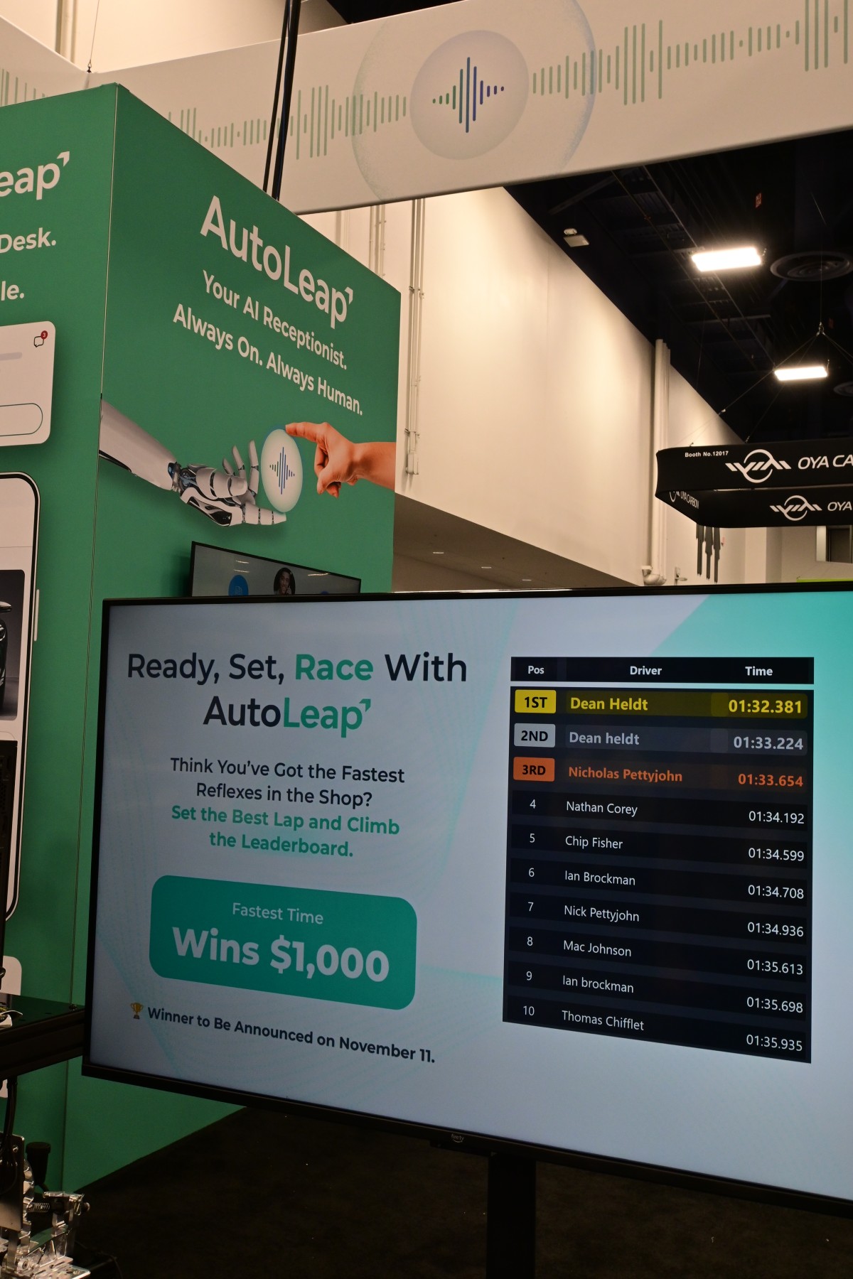 F1 simulator leaderboard in front of the AutoLeap AIR AI receptionist display at SEMA 2025
